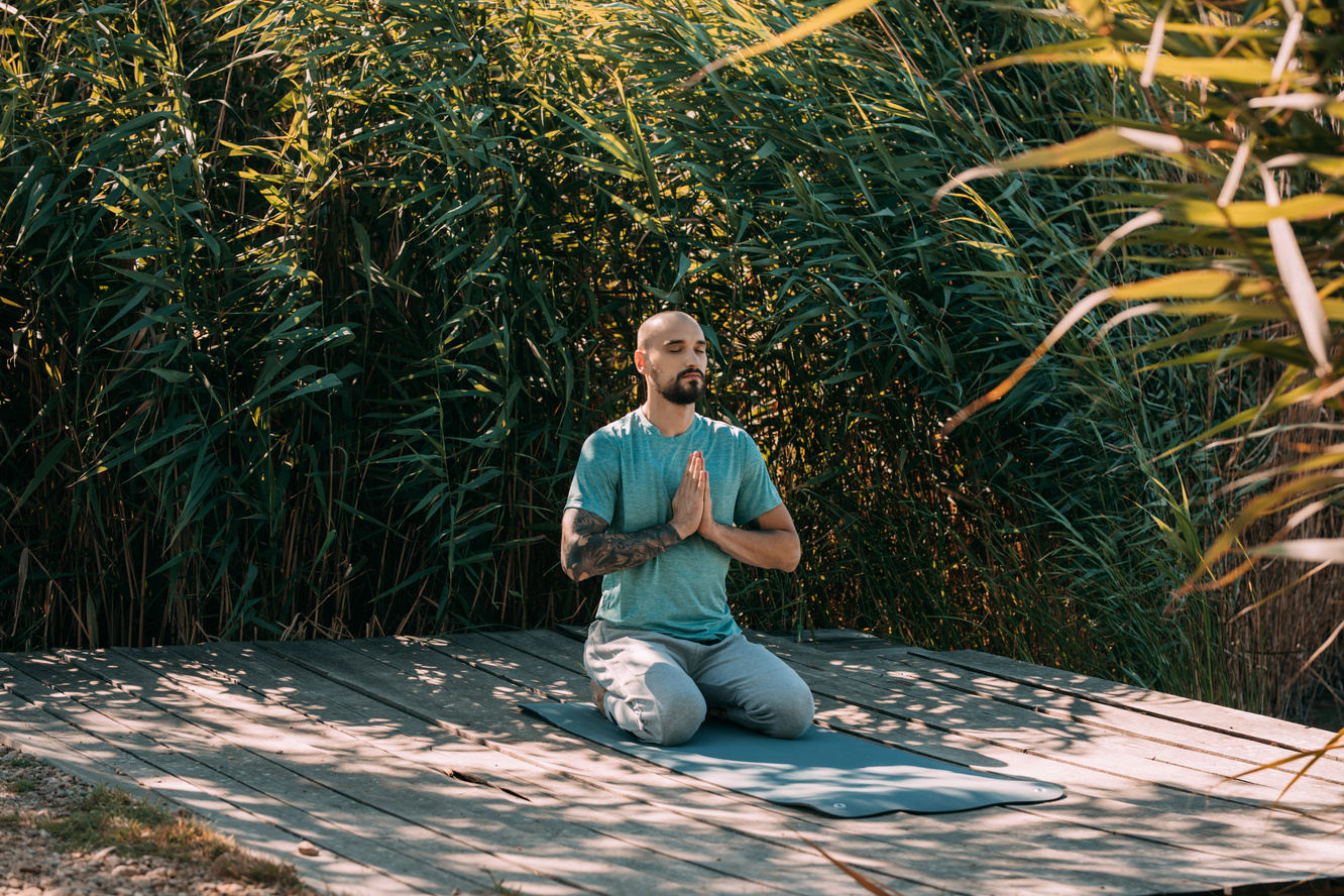 Young Bearded Man Meditating on a Wooden Platform by the Lake, Self Care Concept